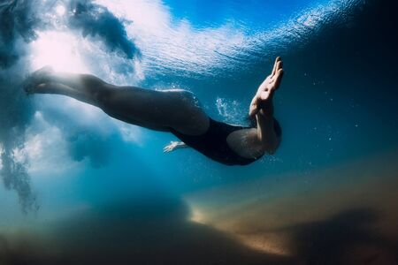 Woman dive without surfboard under ocean wave. Underwater duck dive under wave and sandy bottomの写真素材