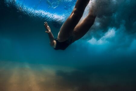 Woman dive without surfboard under ocean wave. Underwater duck dive under wave and sandy bottomの写真素材