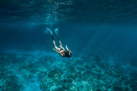 Woman free diver with fins swim underwater in transparent ocean