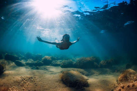 Attractive woman dive near stone with seaweed in underwater. Swimming in blue oceanの写真素材