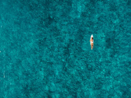 Attractive surfer woman on surfboard in blue ocean. Aerial view