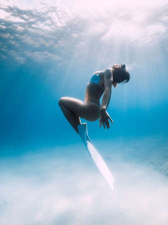 Freediver glides over sandy sea with white fins. Attractive woman free diver in blue oceanの写真素材