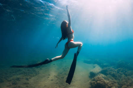 Freediver slim woman in bikini glides in blue sea and sun rays. Freediving with fins underwater in oceanの写真素材