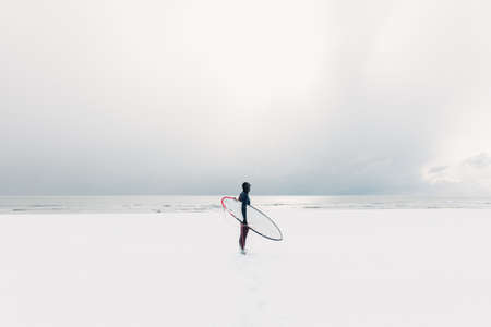 Winter and surfer with surfboard. Snowy beach with male surfer in wetsuit.の写真素材