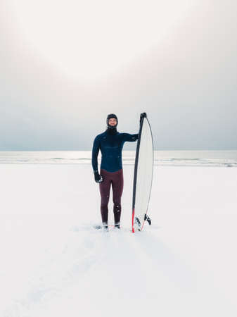 Winter and surfer with surfboard. Snowy beach with male surfer in wetsuit.の写真素材
