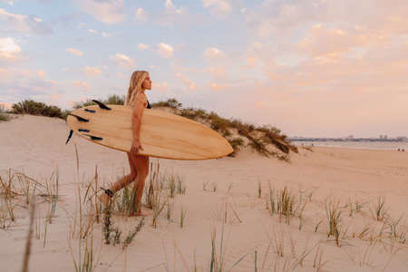 Surfer girl on sand beach with surfboard at warm sunset or sunrise. Attractive surfer women on beach