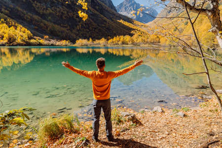 Happy man at the crystal lake in autumnal mountains. Mountain lake and hiker traveler