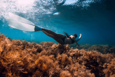 Freediver girl with white fins glides underwater with amazing sun rays and seaweed. Freediving underwater in blue seaの写真素材
