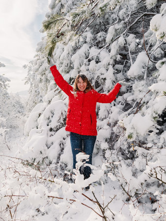 Happy woman standing among snowy trees in winter forest. Traveler woman play with snow