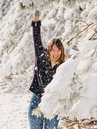 Young woman in red jacket among snowy trees in winter forest. Traveler woman with snow trees in sunny dayの写真素材