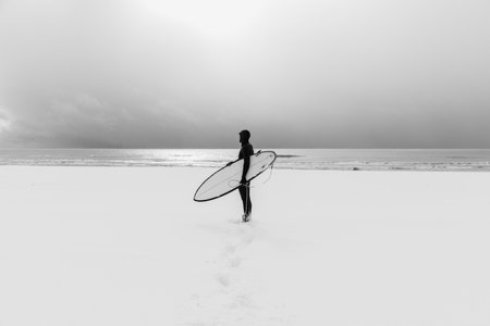 Winter and surfer with surfboard. Snowy beach and surfer in wetsuit.の写真素材