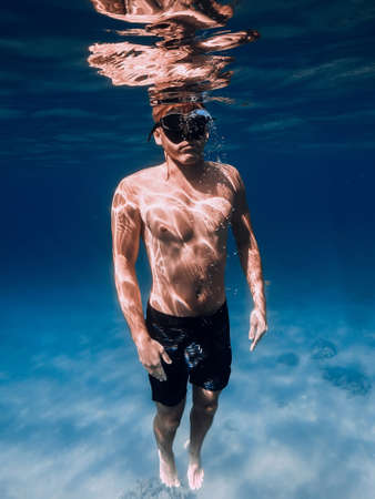 Sporty man freediver stay with fins on sandy bottom underwater in tropical sea.