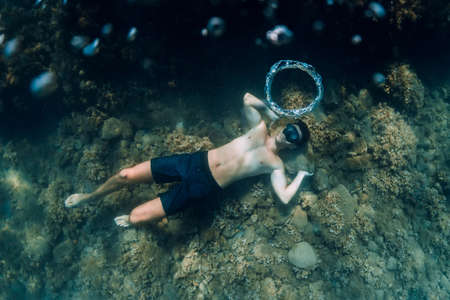 Sporty man freediver stay with fins on sandy bottom underwater in tropical sea.
