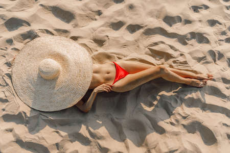 Attractive woman in bikini with big straw hat posing at sandy beach. Woman at vacationsの写真素材