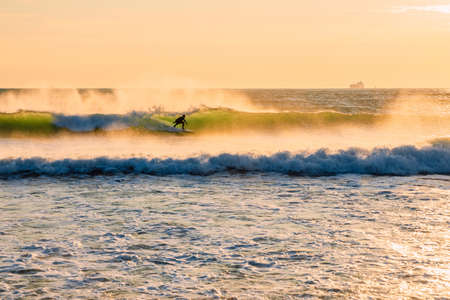 Surfer ride on wave with warm tones of sunset. Surfing in ocean at wavesの写真素材
