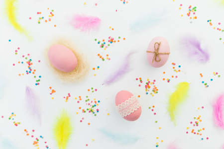 Ester composition with colorful eggs, feathers and confetti on white background. Flat lay, top view
