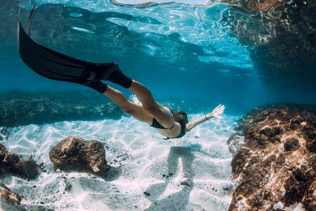 Freediving underwater in blue ocean. Sporty woman freediver swim with fins and corals.の写真素材