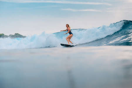 March 11, 2021. Bali, Indonesia. Surfer on surfboard and blue wave. Woman in ocean during surfing.