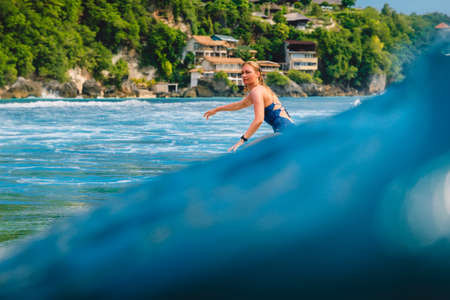March 11, 2021. Bali, Indonesia. Surfer on surfboard and blue wave. Woman in ocean during surfing.