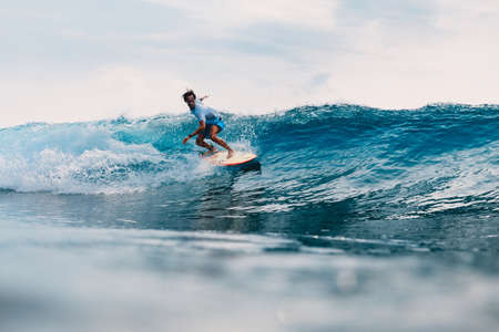 March 11, 2021. Bali, Indonesia. Surfer on surfboard and blue wave. Woman in ocean during surfing.のeditorial素材