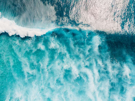 Aerial view of surfers in tropical blue ocean with waves at Bali island. Top view