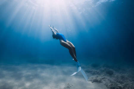 Lady freediver with fins posing and glides underwater in blue ocean with sunlight.の写真素材