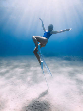 Lady freediver with fins posing and glides underwater in blue ocean with sunlight.の写真素材