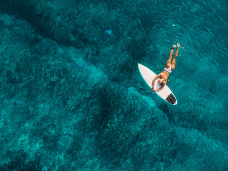 Surfer woman in swimwear hold surfboard at tropical beach with sunset or sunrise tonesの写真素材
