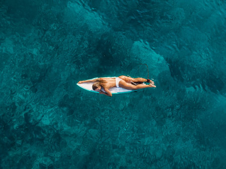 Surfer woman in swimwear hold surfboard at tropical beach with sunset or sunrise tonesの写真素材