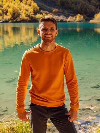 Hiker man at the crystal lake in autumnal mountains. Mountain lake and hiker traveler