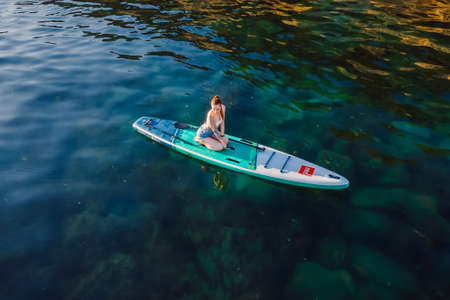 May 27, 2021. Anapa, Russia. Woman on stand up paddle board at blue sea. Traveling on Red paddle sup board in sea. Aerial viewのeditorial素材