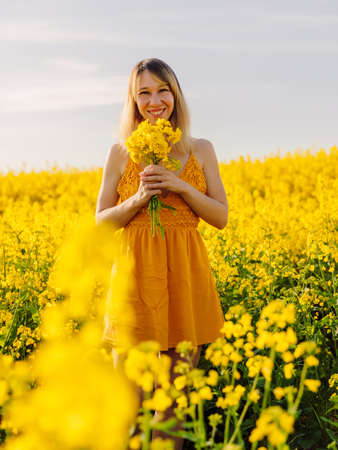 Attractive cheerful woman on rapeseed field with sunset light. Yellow flowers and happy womanの写真素材