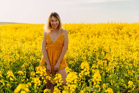 Attractive cheerful woman on rapeseed field with sunset light. Yellow flowers and happy caucasian...