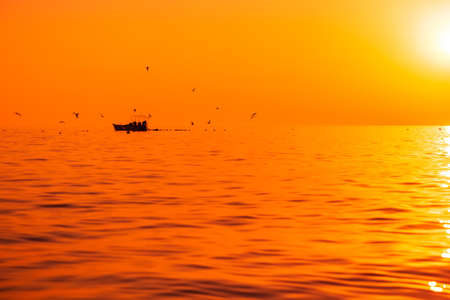 Bright sunset or sunrise at quit ocean with fishing boat and birdsの写真素材