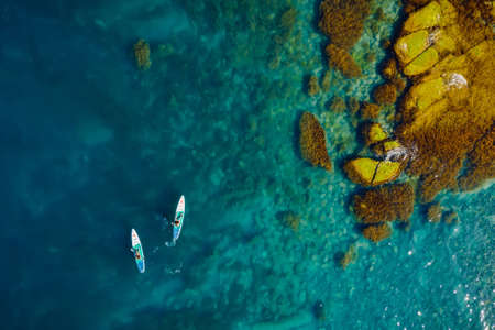 May 28, 2021. Anapa, Russia. Couple on stand up paddle board at blue sea with rocks. People on Red paddle sup board in transparent sea. Aerial viewのeditorial素材