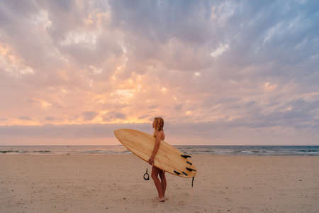 Alone surfer woman on beach with warm sunset tones. Attractive surf girl with surfboard