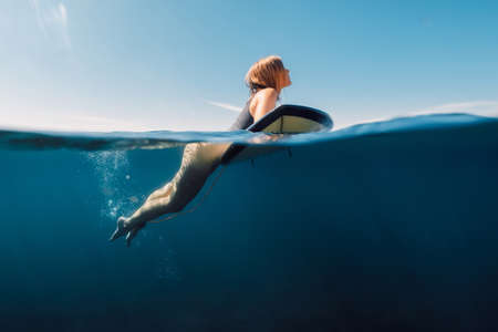 Surf girl rowing on surfboard. Attractive surfer woman in ocean and sunny day