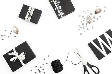 Christmas frame of stylish black gifts with twine, silver cofetti and scissors on white background....
