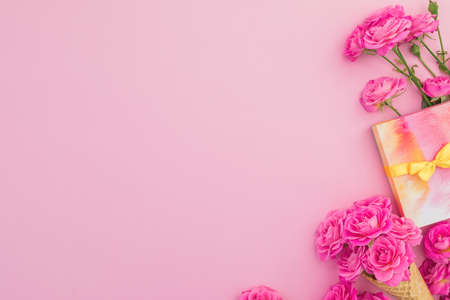 Floral frame of pink roses flowers with gift on pink background. Flat lay, top view