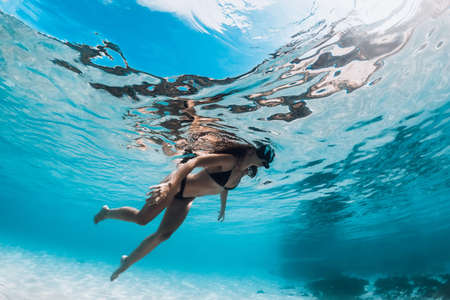 Woman in bikini and with diving mask swimming underwater in tropical transparent ocean with white sand bottomの写真素材