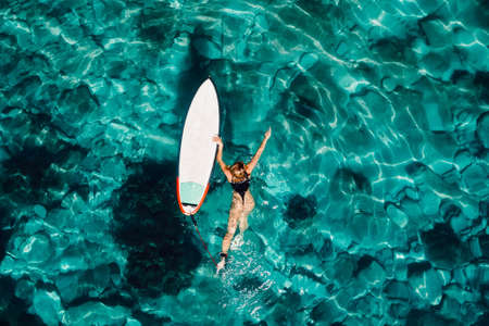 Surf girl swim with surfboard in transparent ocean. Aerial top viewの写真素材