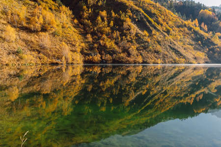 Mountain lake with reflection on surface, autumnal trees and mountainsの写真素材