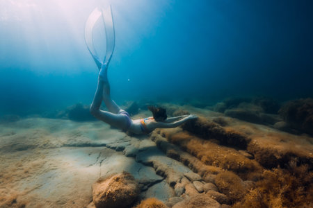August 07, 2021. Varna, Bulgaria. Sporty woman with freediving fins posing underwater in ocean with sunlight. Young girl in colorful bikini glides underwater.の写真素材