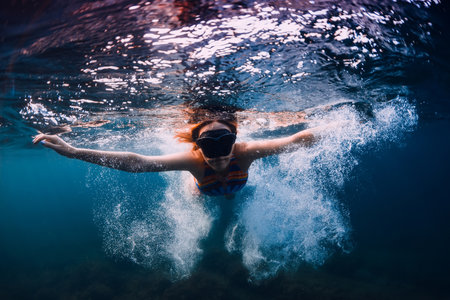 August 07, 2021. Varna, Bulgaria. Sporty woman with freediving fins posing underwater in ocean with sunlight. Young girl in colorful bikini glides underwater.の写真素材