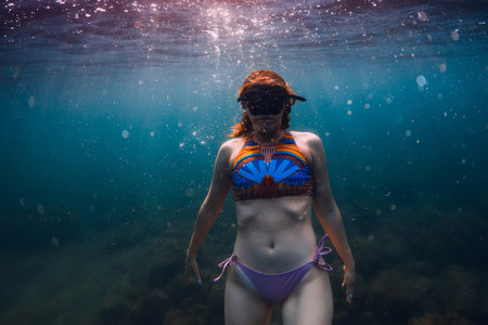 August 07, 2021. Varna, Bulgaria. Sporty woman with freediving fins posing underwater in ocean with sunlight. Young girl in colorful bikini glides underwater.の写真素材