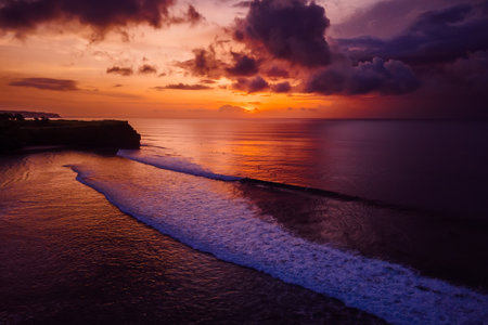 Aerial view of ocean with waves and colorful sunset or sunrise in Bali.