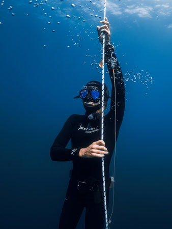 October 03, 2022. Amed, Indonesia. Men in wetsuit with mask and fins training dive on deep in blue ocean. Professional free diver comes to the surface underwater in transparent seaのeditorial素材