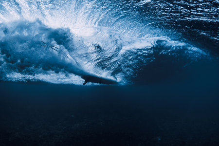 Wave underwater and surfer ride on surfboard in ocean. Underwater crashing wave and surfboard in transparent waterの写真素材