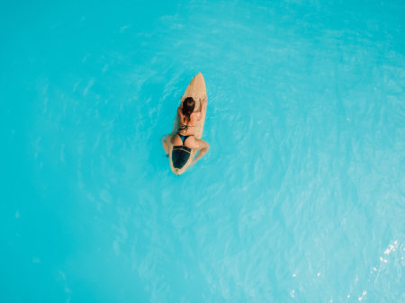 Sexy Surfer girl in bikini waiting wave on surfboard in blue ocean. Aerial view of woman during...