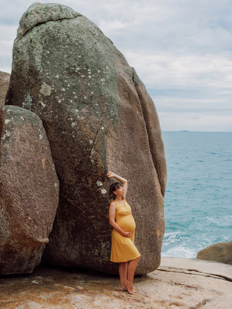 Pregnant woman in yellow dress posing at ocean coastlineの写真素材